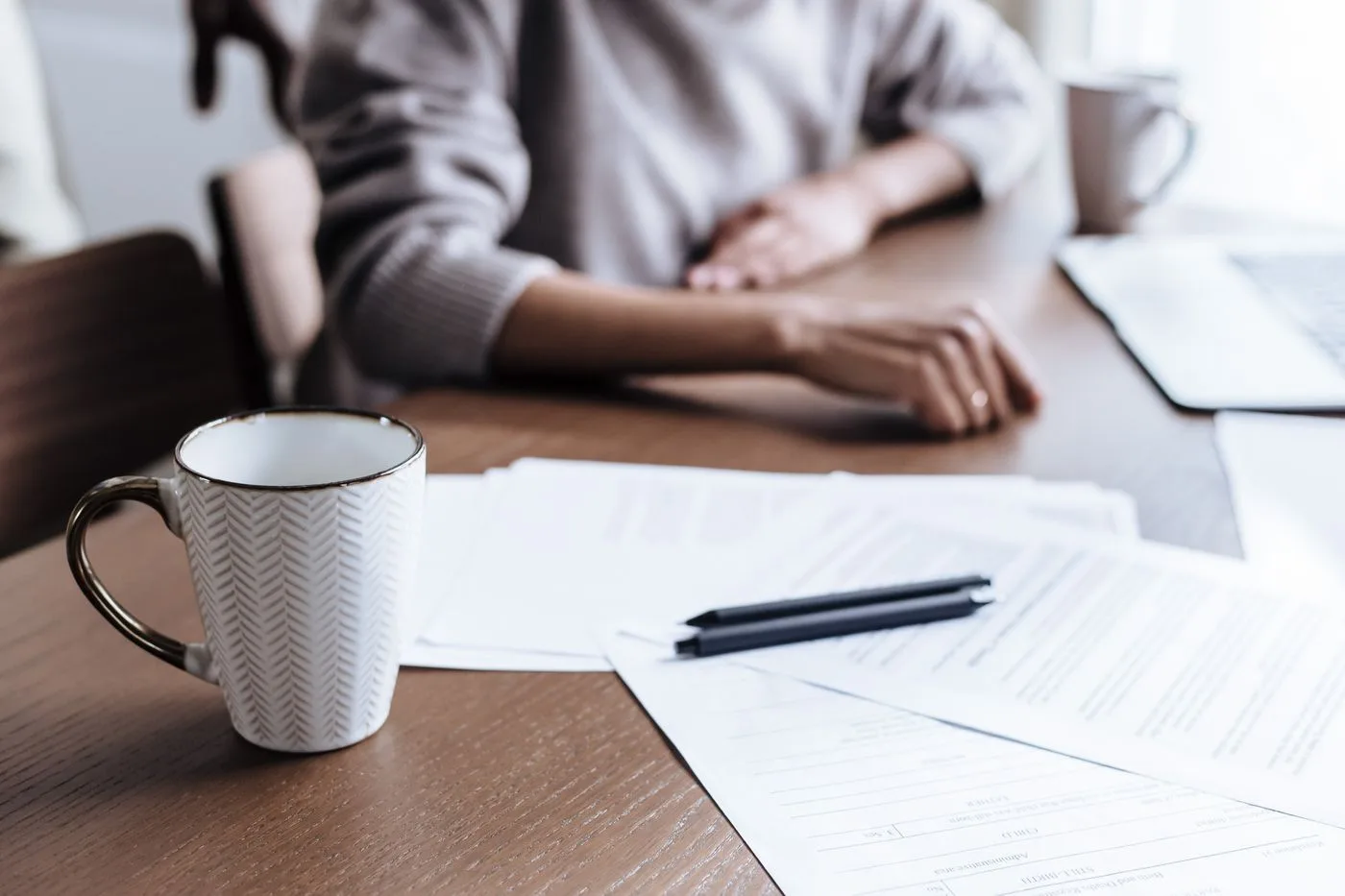 Iemand werkt thuis aan een bureau met administratie en een kopje koffie